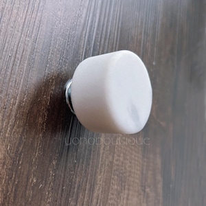 Könnte beinhalten: Weißer Marmorknauf für Schränke mit silberner Basis. Der Knauf ist rund und hat eine glatte Oberfläche.