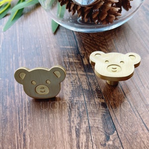 May include: Two gold-toned bear-shaped cabinet knobs with a simple, cartoon-like design.