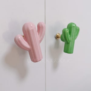 Può includere: Due tiretti per cassetti in ceramica a forma di cactus. Uno è rosa e l'altro è verde.
