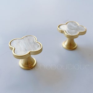 May include: Two gold cabinet knobs with a white, pearlescent, four-leaf clover design.