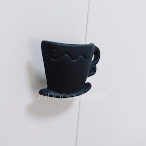 Op de afbeelding: Zwarte keramische theekop-kastknop met een decoratief ontwerp.