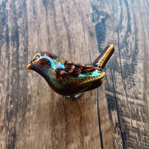 May include: A ceramic bird figurine with brown, green and blue glaze. The bird has a long tail and a small beak.