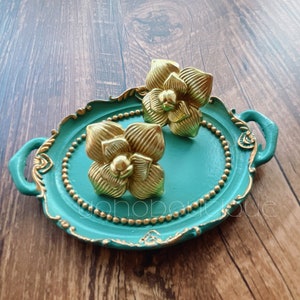 Puede incluir: Dos tiradores de cajones decorativos en forma de flor de color dorado sobre una bandeja azul turquesa con ribetes dorados.