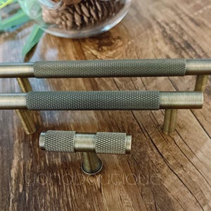 May include: Three antique gold cabinet knobs with a textured finish. The knobs are in a horizontal line with the top knob slightly offset to the right. The knobs are on a wooden surface.