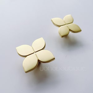 Op de afbeelding: Twee gouden metalen kastknoppen in de vorm van een klavertjevier.