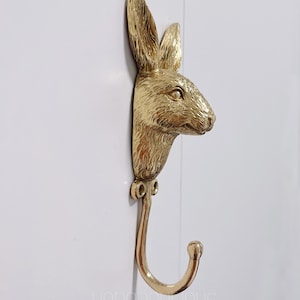 以下が含まれることがあります： 金色のウサギの頭の壁掛けフック。フックはウサギの首に付けられており、丸みを帯びた先端に向かって下に曲がっています。