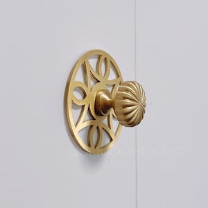 May include: A gold-toned door knob with a decorative, circular, openwork backplate. The knob has a fluted design.