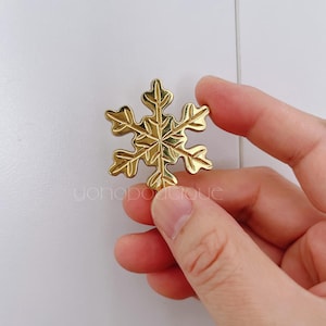 Pode incluir: Um ornamento de floco de neve dourado com detalhes intrincados. O floco de neve é segurado na mão.