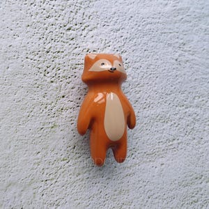 Könnte beinhalten: Eine Keramikfigur eines Fuchses mit einem lächelnden Gesicht. Der Fuchs ist orange mit einem weißen Bauch und steht aufrecht.