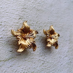 Peut inclure: Une paire de boucles d'oreilles en forme de fleur dorées. Les boucles d'oreilles sont en métal et présentent un design détaillé.
