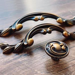 May include: Two ornate, antique-style cabinet pulls with a leaf design. The pulls are made of metal and have a dark brown finish. A matching knob is also included.