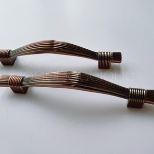May include: Two antique copper cabinet door pulls with a ribbed design. The pulls are curved and have a decorative end cap.