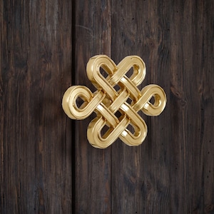 以下が含まれることがあります： 濃い木製の表面に、伝統的な中国の結び目に似た、金色の金属製の結び目のデザインが取り付けられています。