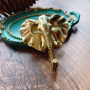 May include: A gold-colored elephant figurine with a textured surface, sitting on a teal-colored tray with gold accents.