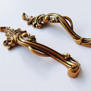 Puede incluir: Dos tiradores de cajón de metal dorado adornados con un diseño decorativo en espiral.