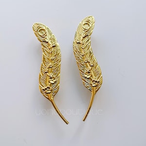 Puede incluir: Dos pinzas para el pelo doradas en forma de pluma con un diseño floral.