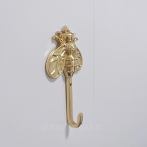 May include: Gold bee-shaped hook with a J-shaped hook at the bottom. The bee has a textured body and wings.