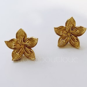 Op de afbeelding: Een paar gouden oorbellen in de vorm van een bloem. De oorbellen zijn gemaakt van metaal en hebben een gedetailleerd ontwerp.