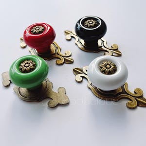 May include: Four ceramic cabinet knobs with ornate gold metal bases. The knobs are in black, red, green, and white with a gold flower design in the centre.