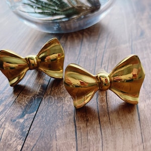 以下が含まれることがあります： 金色の蝶ネクタイの形をした装飾的な引き出しの取っ手が2つあります