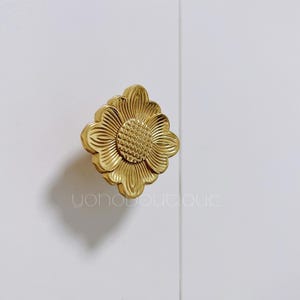 Pode incluir: Uma maçaneta de armário em forma de flor de cor dourada com um design detalhado.