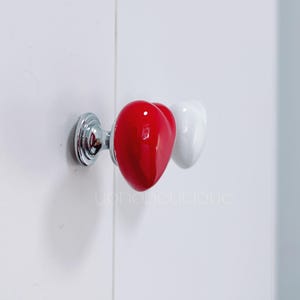 May include: A set of two heart-shaped cabinet knobs, one red and one white. The knobs are attached to a silver metal base.