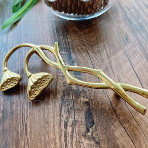 Könnte beinhalten: Goldfarbener Metall-Schrankbeschlag mit einem stilisierten Ast-Design und zwei lotusblütenförmigen Griffen.