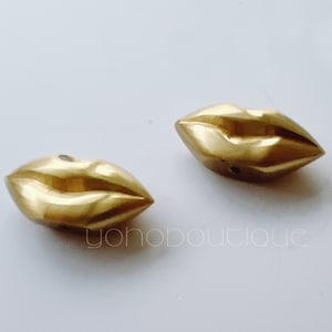 May include: Two gold-coloured metal lips charm pendants. The lips are detailed and have a smooth, shiny finish.