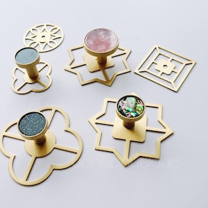 以下が含まれることがあります： 異なる形のベースと装飾的なインレイが付いた、5つの金色の金属製のフック。インレイには、ピンクの石、黒い石、真珠貝の貝殻、そして2つのキラキラ光る黒い石が含まれています。