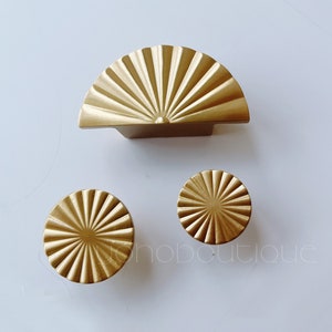 Può includere: Tre pomelli per armadi dorati con un design a forma di sole. Il pomello più grande è a forma di semicirconferenza, mentre i due pomelli più piccoli sono rotondi.