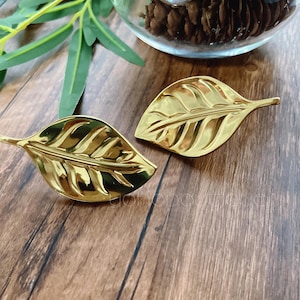 May include: Two gold leaf-shaped metal hair clips. The clips are shiny and have a textured surface.