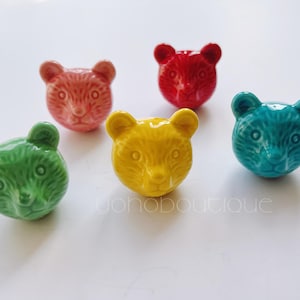 Pode incluir: Cinco estatuetas de cerâmica em forma de urso em diferentes cores: verde, rosa, amarelo, vermelho e azul. Cada urso tem um rosto simples e de estilo de desenho animado.