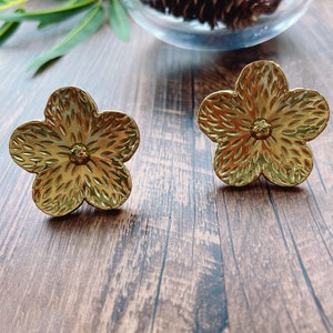 Puede incluir: Un par de pendientes de oro en forma de flor con una superficie texturizada.