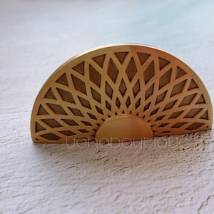 Op de afbeelding: Een gouden metalen kastknop met een geometrisch zonnestralenontwerp. De knop is halfrond.