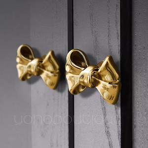 Op de afbeelding: Twee gouden, boogvormige kastknoppen met een gestructureerd oppervlak.