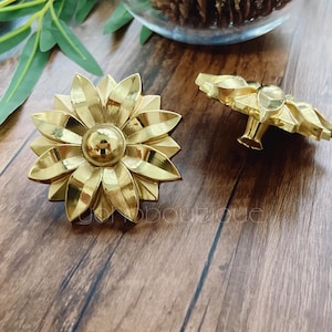 Pode incluir: Dois puxadores de gaveta de metal dourado em forma de flor. Os puxadores têm um design detalhado com várias pétalas.