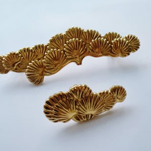 May include: Two gold metal decorative door pulls shaped like pine branches with detailed fan-shaped leaves.