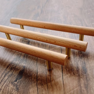 May include: Three wooden cabinet pulls with gold metal hardware. The pulls are arranged in a stack, with the top pull slightly offset from the others.