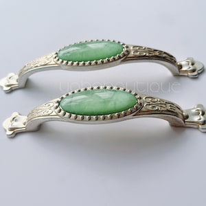 May include: Two silver cabinet knobs with ornate detailing and oval green glass inserts.