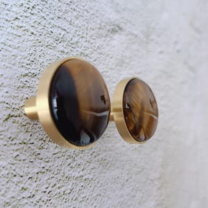 Op de afbeelding: Twee ronde, goudkleurige kastknoppen met inleg van tijgeroog.