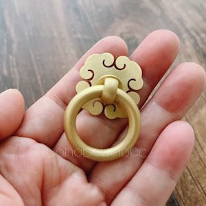 May include: Gold-toned metal cabinet knob with a decorative cloud-shaped design and a ring pull.