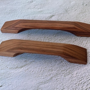 Pode incluir: Duas puxadores de porta de armário de madeira com acabamento em madeira natural. As puxadores são curvas e têm um design simples.