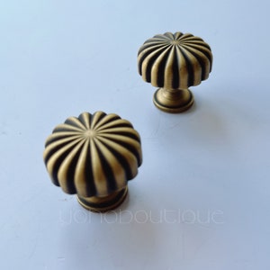 Op de afbeelding: Twee messing kastknoppen met een geribbeld ontwerp. De knoppen zijn donkergoud van kleur met zwarte accenten.