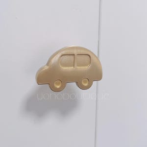 May include: Gold car-shaped cabinet knob. The knob is a simple design with a rounded shape and a small window in the front.