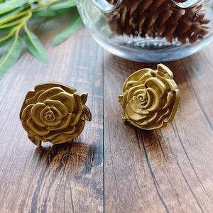 May include: Two gold-toned rose-shaped drawer pulls. The pulls are detailed with a raised, textured design.