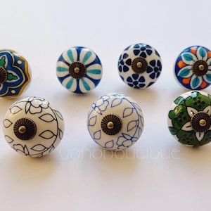 Pode incluir: Conjunto de oito botões de cerâmica com vários padrões florais azuis, verdes e brancos. Cada botão tem um acento metálico dourado no centro.