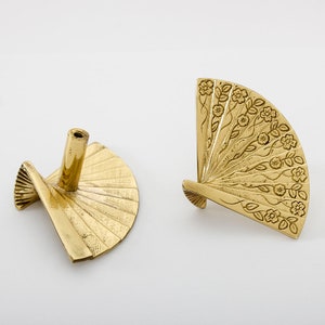 Könnte beinhalten: Zwei goldfarbene Metall-Schrankknöpfe in Form eines Fächers mit floralem Design. Die Knöpfe sind dekorativ und im traditionellen asiatischen Stil gehalten.