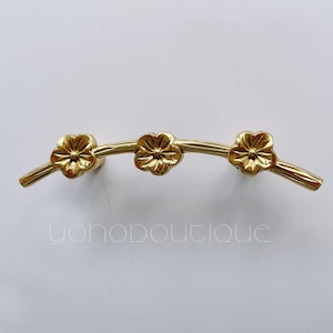 May include: Gold-toned cabinet hardware with a floral design. The hardware features three stylized flower shapes on a curved branch.