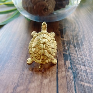 Op de afbeelding: Een gedetailleerd, goudkleurig schildpadfiguur met een getextureerd schild en poten. De schildpad staat op een houten oppervlak, met een vage achtergrond met groen en een glazen bol. Het beeldje is een decoratief item.