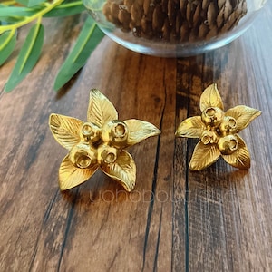 Peut inclure: Une paire de boucles d'oreilles dorées en forme de fleur à cinq pétales et un groupe de baies au centre.